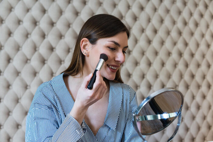 Young woman smiling while applying makeup with a brush, illustrating childish reasons ladies ditched a guy concept.