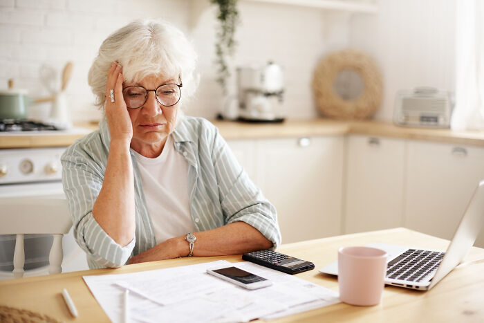 Elderly woman looking confused at bills and a laptop, reflecting on mind-boggling conversations with adults.