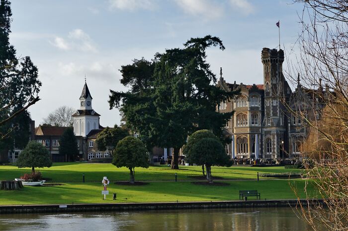 Historic iconic TV house with clock tower and castle-style architecture beside a river and green lawn in real life.