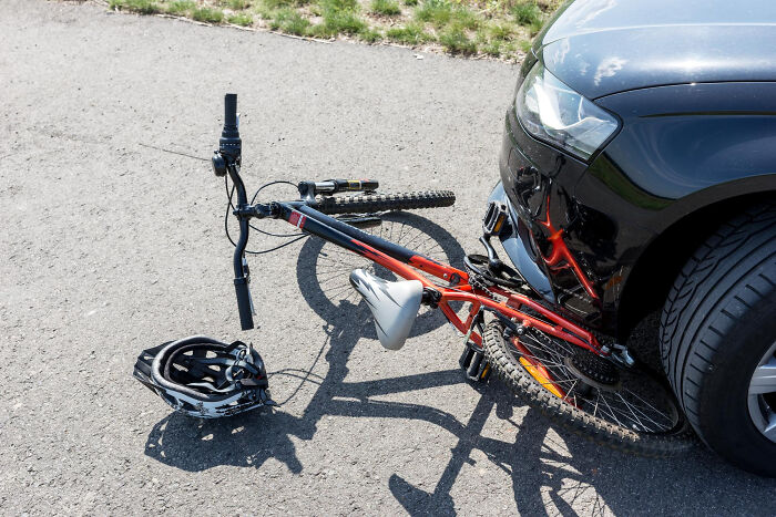 Red bicycle crushed under the front bumper of a black car after a collision, highlighting shocking school incidents.