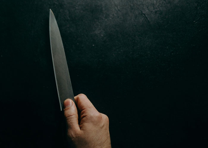 Hand holding a sharp knife against a dark background illustrating terrifying true stories that are hard to believe.