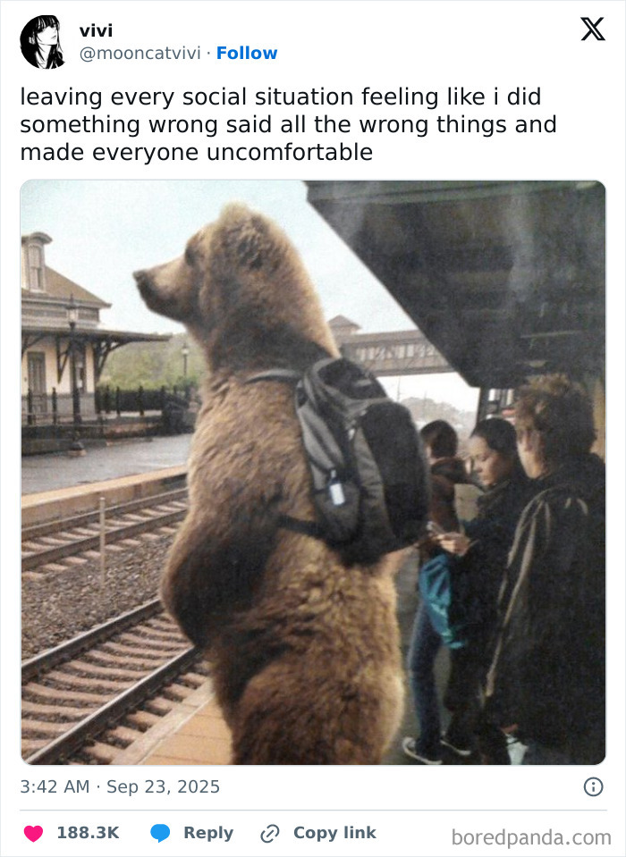 A bear wearing a backpack stands at a train station platform among waiting passengers, funny tweets of September.