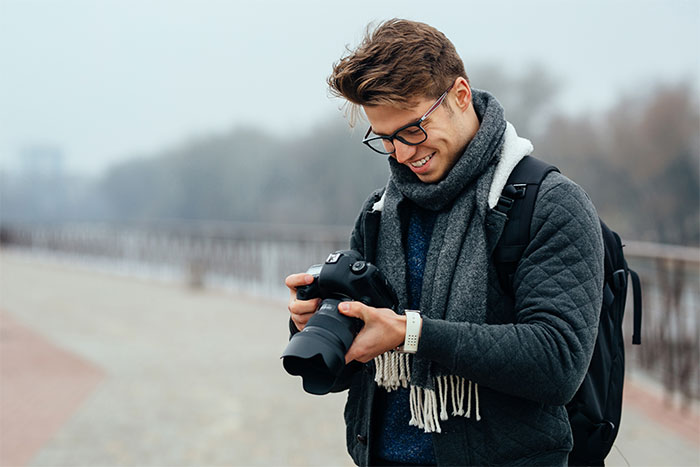 Young man holding a camera outdoors, smiling while reviewing photos, illustrating a story about catching a friend stealing. Young man holding a camera outdoors, smiling while reviewing photos, illustrating a story about catching a friend stealing.