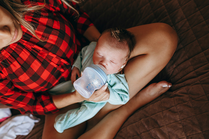 Woman feeding baby with bottle while sitting on bed, reflecting on marriage and life sacrifices for a child. Woman feeding baby with bottle while sitting on bed, reflecting on marriage and life sacrifices for a child.