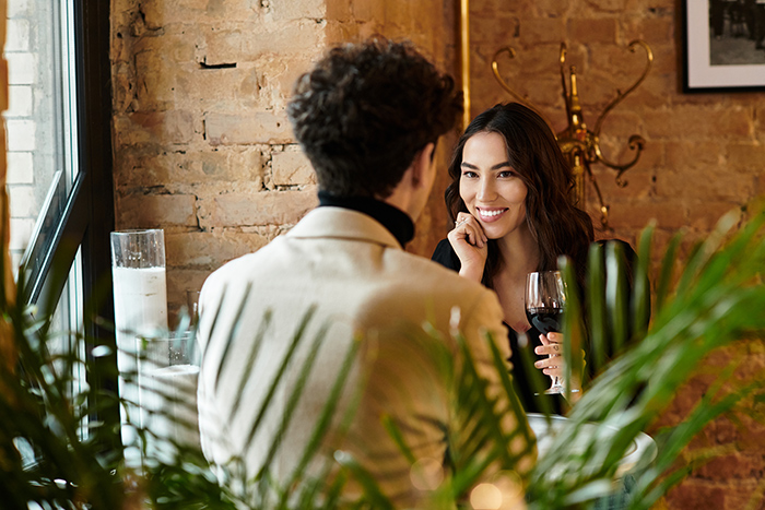 Woman and man on a date in a cozy restaurant, with the woman smiling and holding a glass of red wine. Woman and man on a date in a cozy restaurant, with the woman smiling and holding a glass of red wine.