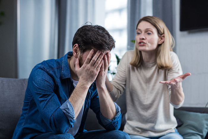 Man and woman having a heated argument on couch, illustrating a man jokes about trading wife for younger woman concept. Man and woman having a heated argument on couch, illustrating a man jokes about trading wife for younger woman concept.