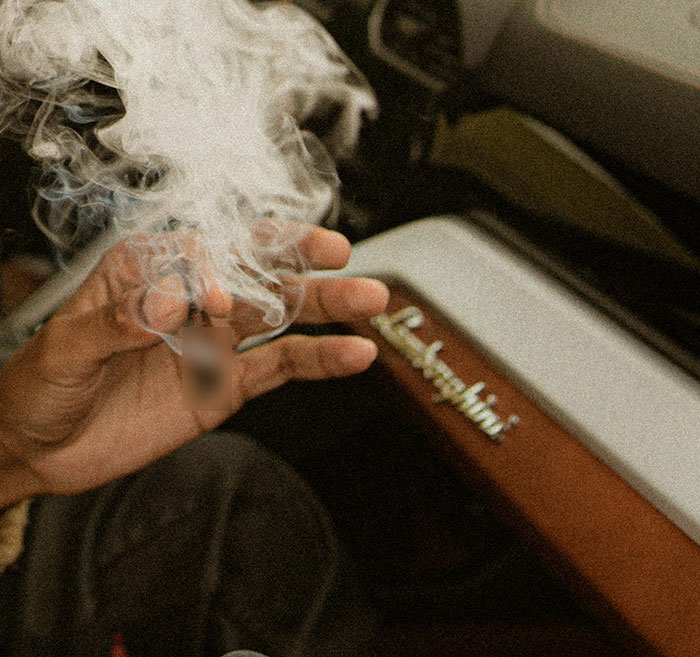 Hand holding a smoldering cigarette inside a car with smoke rising, related to hotboxing and child endangerment. Hand holding a smoldering cigarette inside a car with smoke rising, related to hotboxing and child endangerment.