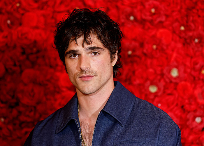 Actor Jacob Elordi posing in front of a vibrant red rose background promoting Wuthering Heights teaser. Actor Jacob Elordi posing in front of a vibrant red rose background promoting Wuthering Heights teaser.