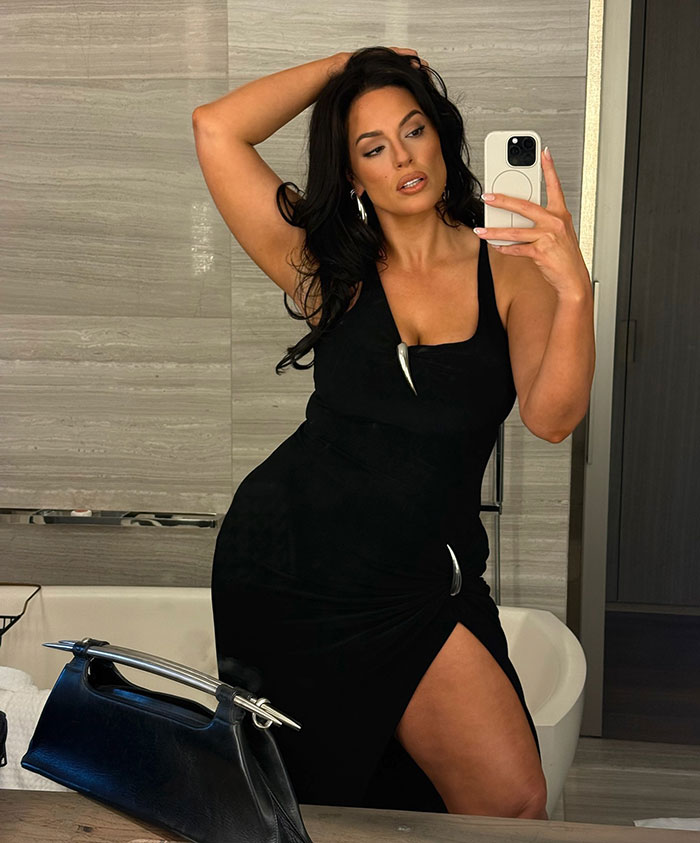 Ashley Graham wearing a body-hugging black dress revealing her figure, taking a mirror selfie in a modern bathroom. Ashley Graham wearing a body-hugging black dress revealing her figure, taking a mirror selfie in a modern bathroom.