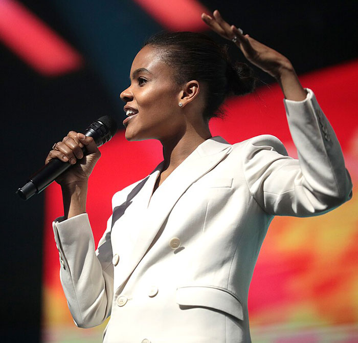 Candace Owens speaking at an event, holding a microphone and gesturing with her hand against a red backdrop. Candace Owens speaking at an event, holding a microphone and gesturing with her hand against a red backdrop.