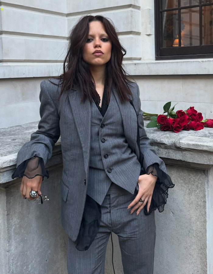 Jenna Ortega in a gray pinstripe suit, posing outdoors with a bouquet of red roses, styled by her Emmy outfit stylist. Jenna Ortega in a gray pinstripe suit, posing outdoors with a bouquet of red roses, styled by her Emmy outfit stylist.