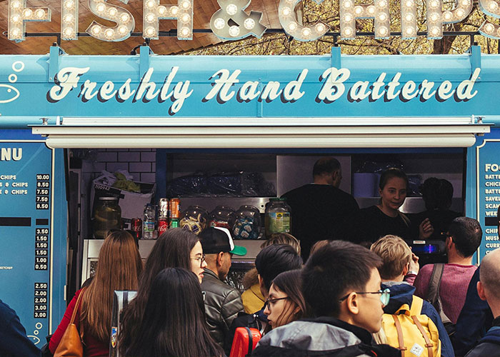 Crowd waiting at a food stand offering fish and chips, highlighting common purchases ditched for high price tags.