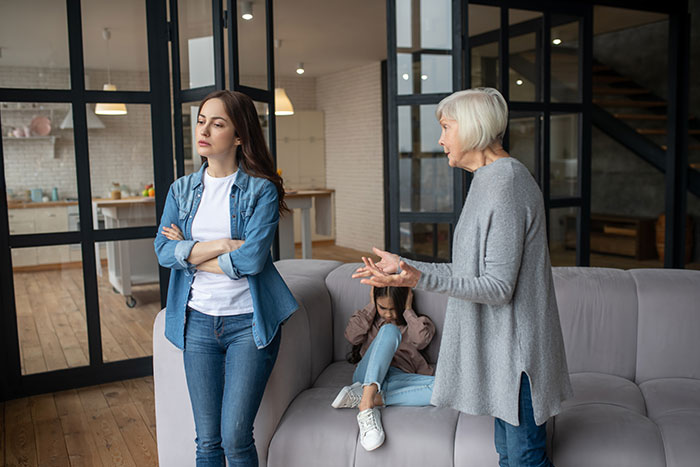 Woman with arms crossed looking upset as older woman talks and child sits on couch in a modern living room. Woman with arms crossed looking upset as older woman talks and child sits on couch in a modern living room.