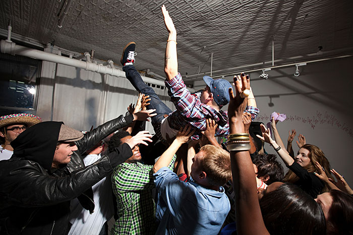 A diverse group of people crowd surfing at a party, symbolizing the inclusion of AI into everything trend.