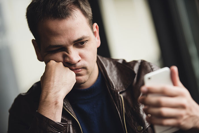 Young man in a leather jacket looking frustrated at smartphone, reflecting challenges with inclusion of AI into everything.