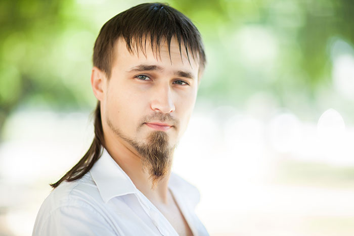 Young man with unique hairstyle and goatee outdoors, symbolizing modern trends and inclusion of AI into everything.