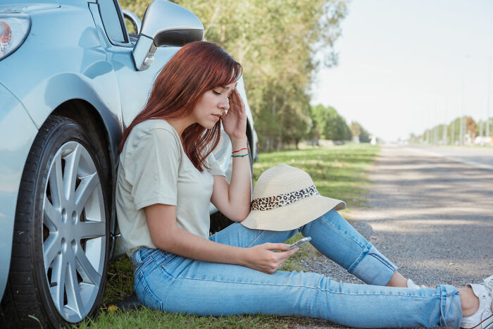 Young woman sitting by a car on a roadside, looking distressed while checking her phone, hinting at shocking school incidents.