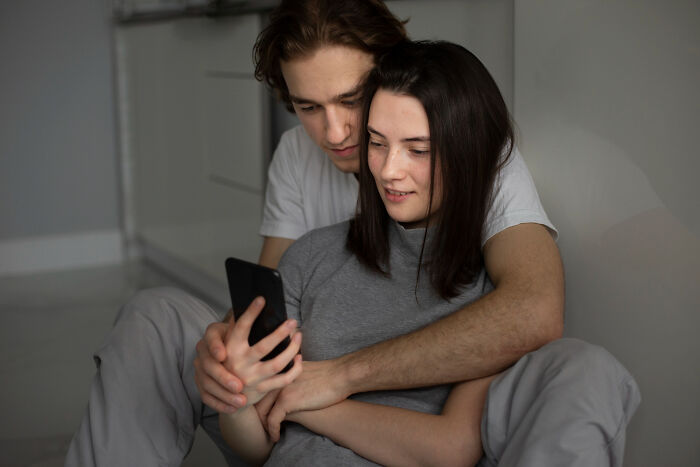 Young couple sitting closely together, looking at a phone, capturing a moment related to falling out of love online.