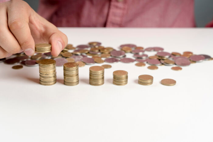 Close-up of a hand stacking coins in ascending order amid scattered change, reflecting mind-boggling conversations with adults.
