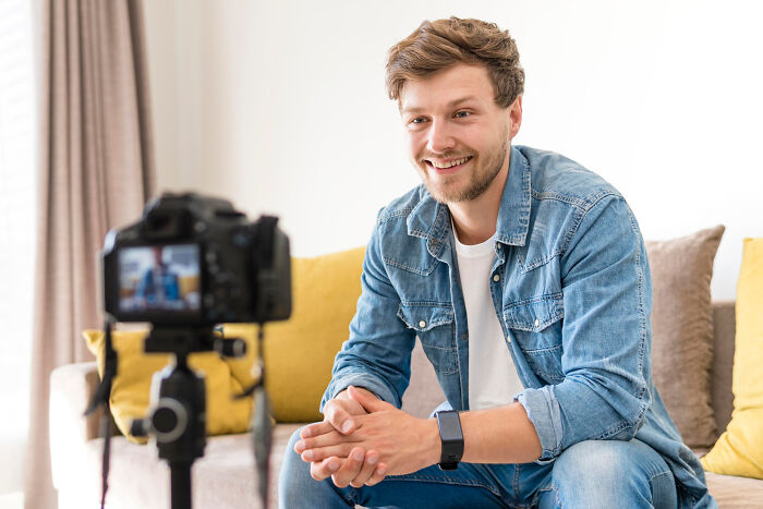 Young man smiling and talking to camera indoors, illustrating childish reasons ladies ditched a guy in casual setting.