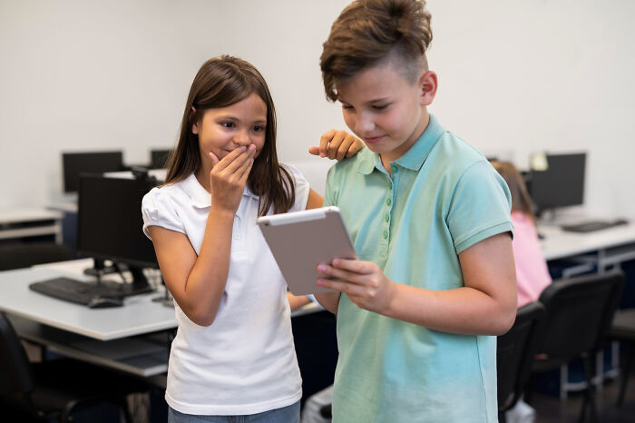 Two school children looking at a tablet with shocked expressions in a classroom, highlighting shocking school incidents.