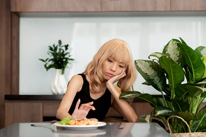 Young woman looking upset at a plate of food, illustrating inlaws push boundaries during divorce situations. Young woman looking upset at a plate of food, illustrating inlaws push boundaries during divorce situations.