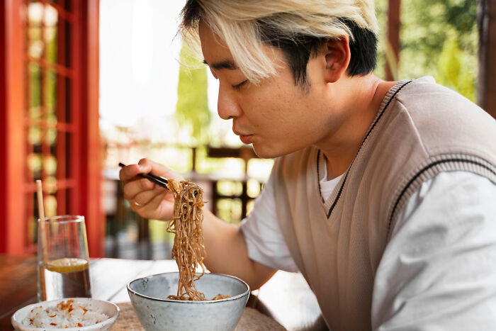 Young man eating noodles at a table outdoors, illustrating childish reasons ladies ditched a guy with avocado reference.