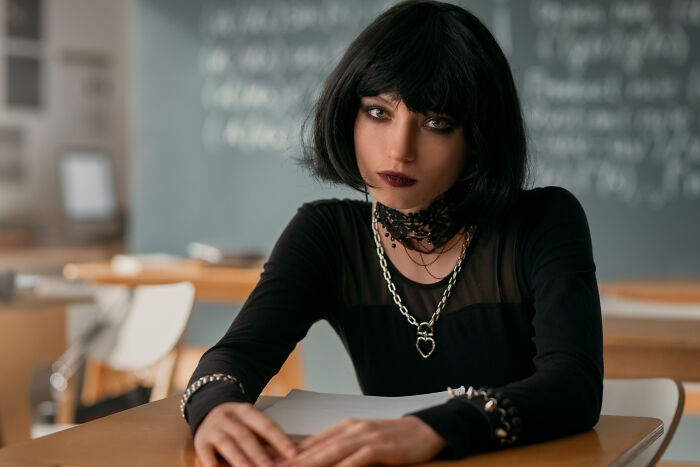 Teen girl with black bob haircut and gothic style sitting at school desk in classroom, representing shocking school incidents.