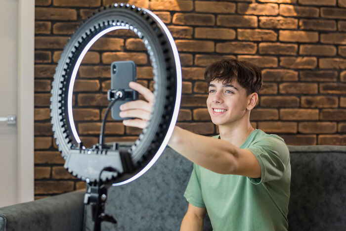 Teen boy taking a selfie with smartphone and ring light, highlighting childish reasons ladies ditched a guy.