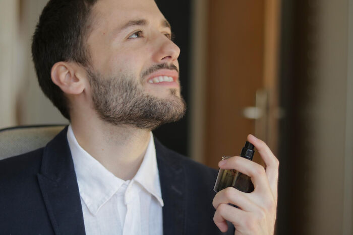 Young man in a blue blazer applying cologne indoors, illustrating childish reasons ladies ditched a guy with avocado question.