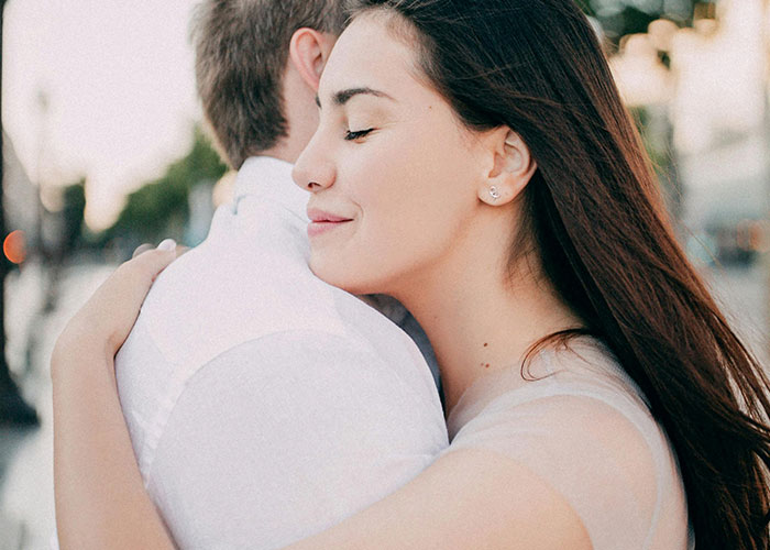 A woman hugging a man who looks uninterested, illustrating men’s perspective on creepy things women do that cross the line.
