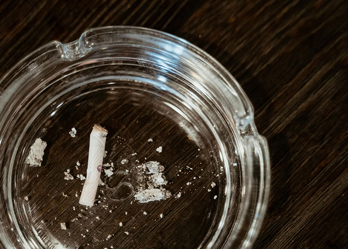Glass ashtray with cigarette b**t and ashes on dark wooden surface, illustrating common purchases ditched due to price tags.