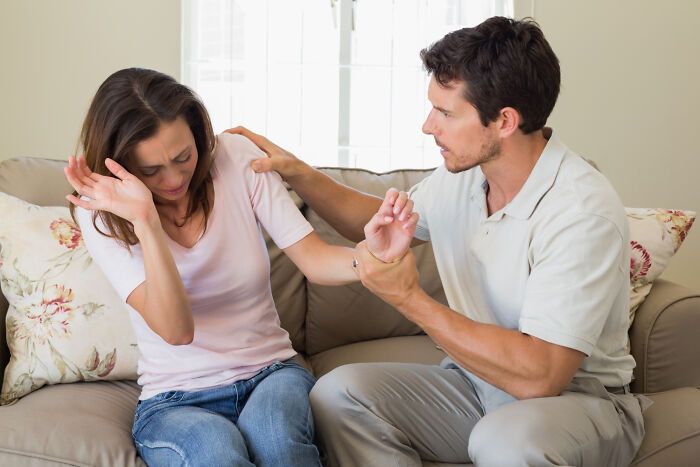 Couple on a couch showing signs of falling out of love, with the woman pulling away and man trying to hold her hand.