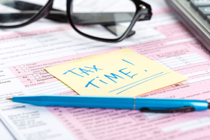 Close-up of tax forms with a blue pen, glasses, and a note saying Tax Time, illustrating mind-boggling adult conversations.