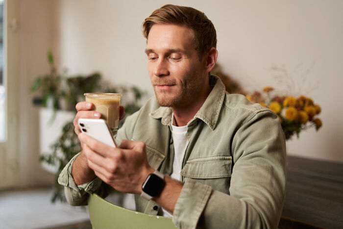 Man with light brown hair in casual jacket drinking coffee and looking at smartphone in a cozy indoor setting about childish reasons dating