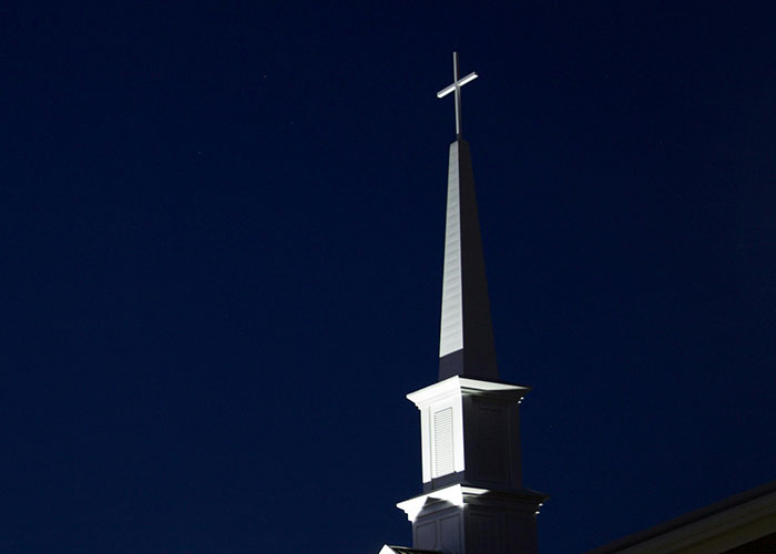 Steeple with illuminated cross against a dark night sky, symbolizing historical events impact on society.