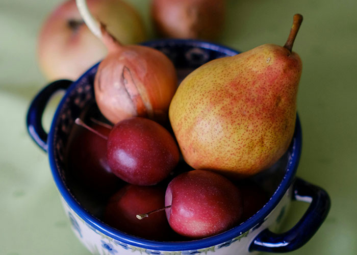 Bowl of fresh fruit including pears and plums representing common purchases people have ditched due to price tags