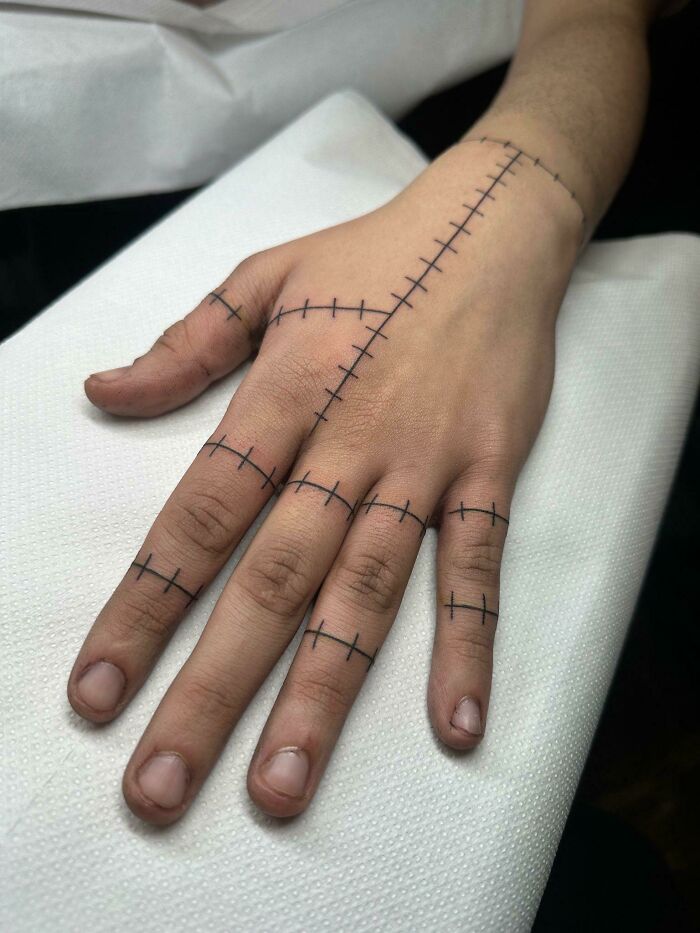 Hand tattoo with black ink lines resembling stitches across fingers and back of hand, illustrating unusual client tattoo requests.