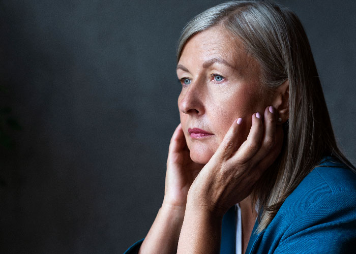 Woman with gray hair in a blue jacket looking pensive, reflecting on feelings related to mother poisoned me experience. Woman with gray hair in a blue jacket looking pensive, reflecting on feelings related to mother poisoned me experience.