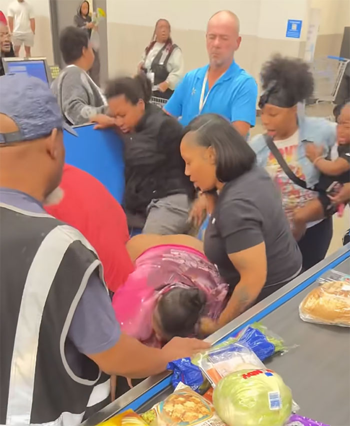 Angry mob surrounding and confronting Walmart employee near checkout with groceries visible on the counter in chaotic scene Angry mob surrounding and confronting Walmart employee near checkout with groceries visible on the counter in chaotic scene
