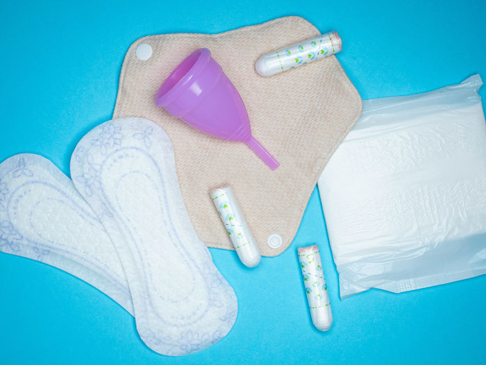 Menstrual hygiene products including pads, tampons, and a menstrual cup on a blue background representing the girl’s health context. Menstrual hygiene products including pads, tampons, and a menstrual cup on a blue background representing the girl’s health context.