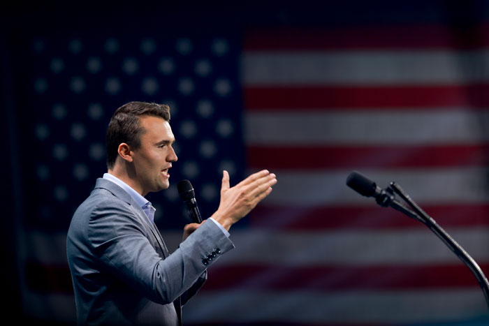 Man in a gray suit speaking into microphone on stage with American flag backdrop, related to Jimmy Kimmel's return news Man in a gray suit speaking into microphone on stage with American flag backdrop, related to Jimmy Kimmel's return news