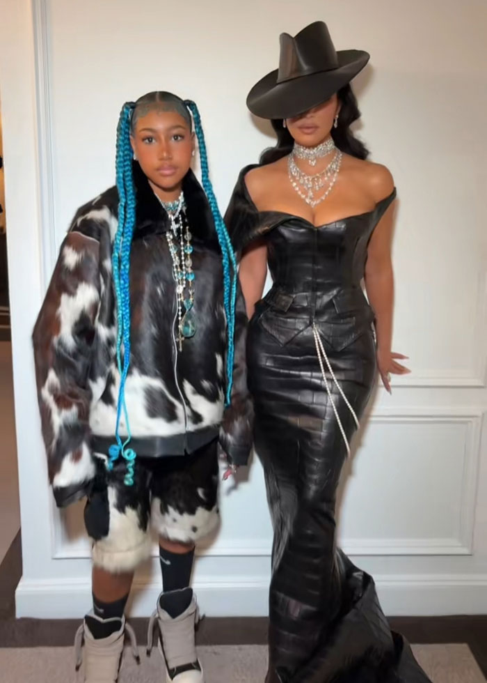 Woman in black leather dress and hat with daughter in cow print outfit and blue braids posing indoors representing Kanye West pain and betrayal list. Woman in black leather dress and hat with daughter in cow print outfit and blue braids posing indoors representing Kanye West pain and betrayal list.