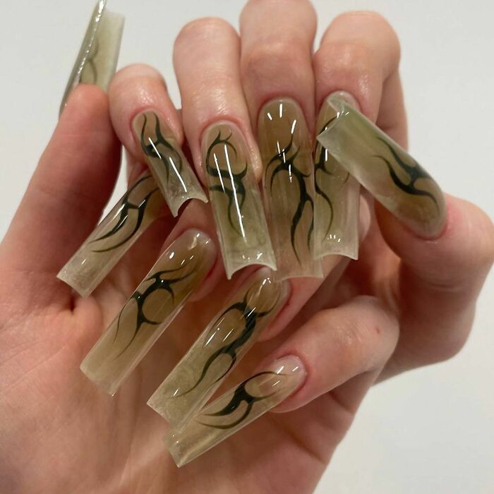 Long clear nails with black flame designs on natural-colored nail beds in a creative and bold nail design style.