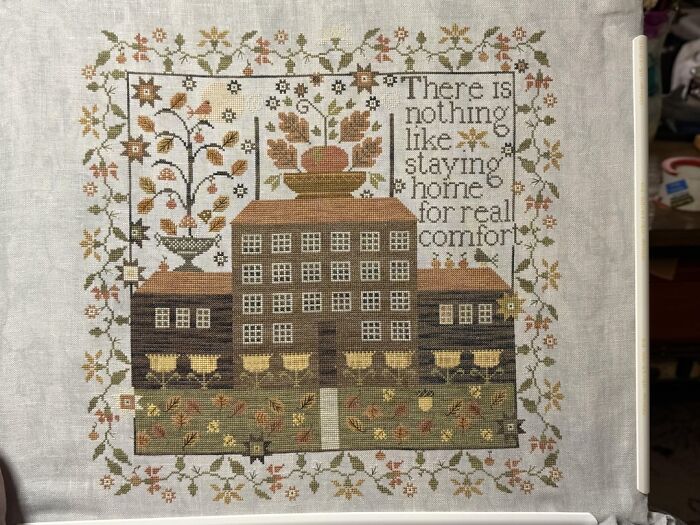Cross-stitch embroidery of a house with a floral border, showcasing one of the things people used to spend hours doing.