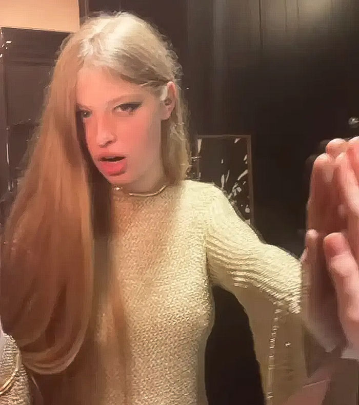 Elon Musk’s transgender daughter with long hair wearing a beige sweater inside a dark room touching a mirror. Elon Musk’s transgender daughter with long hair wearing a beige sweater inside a dark room touching a mirror.