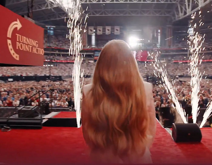 Woman with long hair on stage at a large event with fireworks, related to WWE level stuff and surprising entrance. Woman with long hair on stage at a large event with fireworks, related to WWE level stuff and surprising entrance.