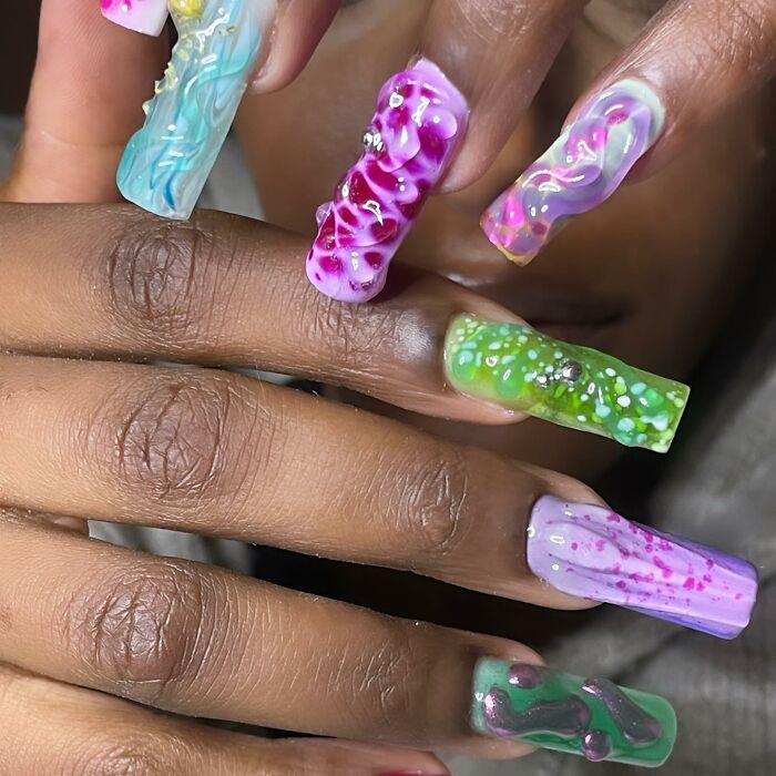 Close-up of hand showing unique 3D textured nail designs in vibrant green, purple, pink, and blue shades.