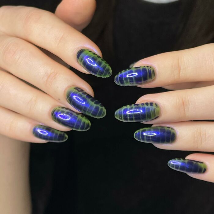 Close-up of hands showing unique blue and green nail designs with a glossy finish, showcasing creative nail art styles.
