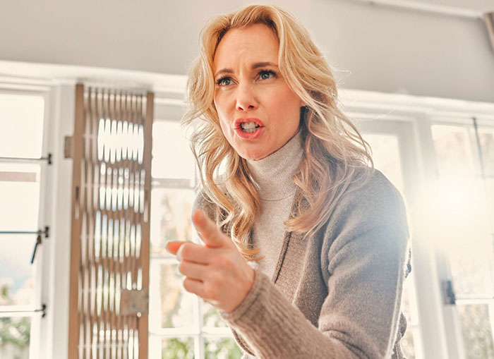 Angry woman pointing finger indoors, highlighting risk of anaphylaxis due to ignoring no-peanut allergy rule at home.